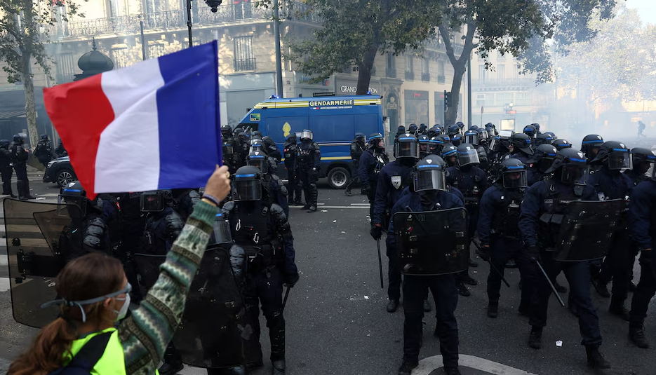 A protester wearing a yellow vest holds a French flag in front of French riot police amid clashes during a day of demonstrations against the cost of living and rising fuel prices in Paris as part of nationwide protests called by the "Yellow Vests" movement, joined by French high school and university students, teachers and parents demanding better school conditions and government action
