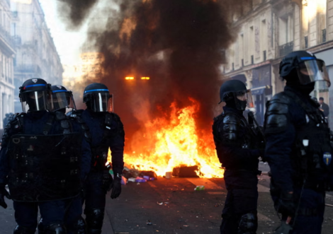 A fire burns as police officers in riot gear stand guard in Paris. Photograph: Abdul Saboor/Reuters