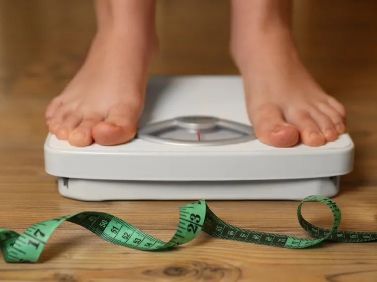 Stock image: someone stands on scales near measuring tape on a wooden floor.
