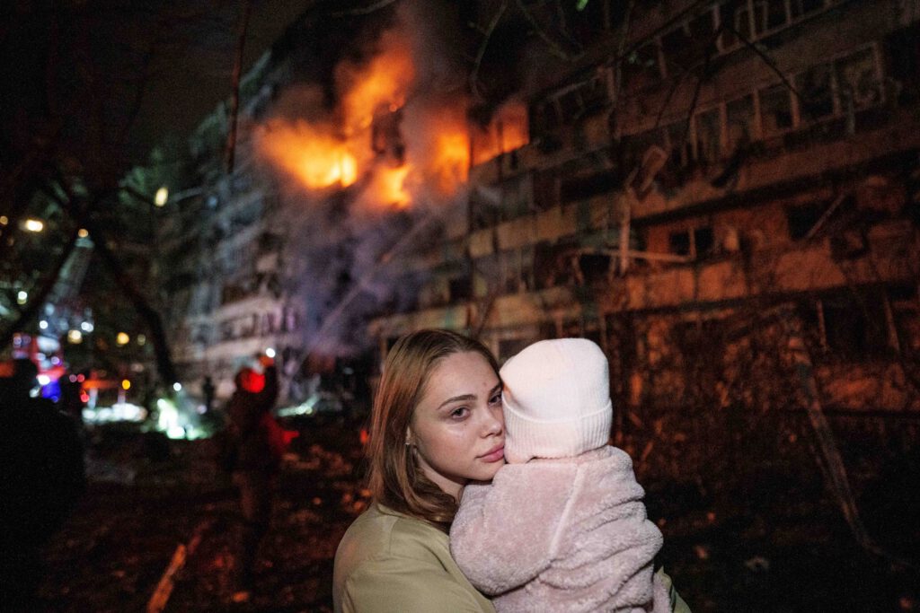A woman holds her daughter in front of a residential building damaged in a Russian missile strike in Kyiv this week. (Evgeniy Maloletka/AP)